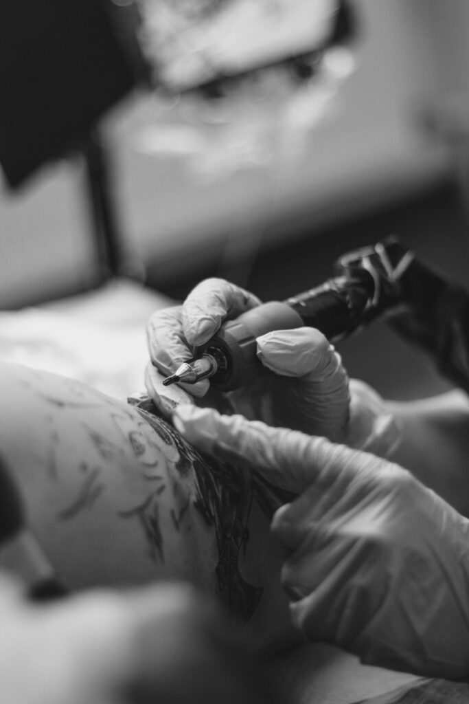 Tattoo arist holding tattoo gun working on client, Tattoo is not recognizeable