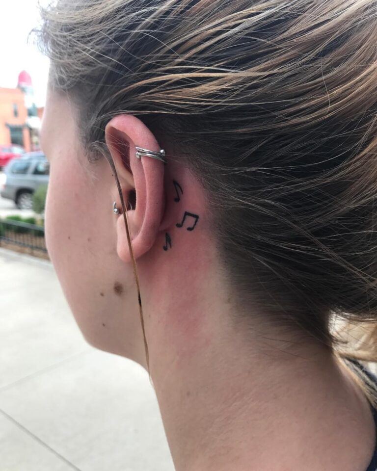 A close-up of a person's neck featuring a small tattoo of music notes near the ear, with earbuds visible.