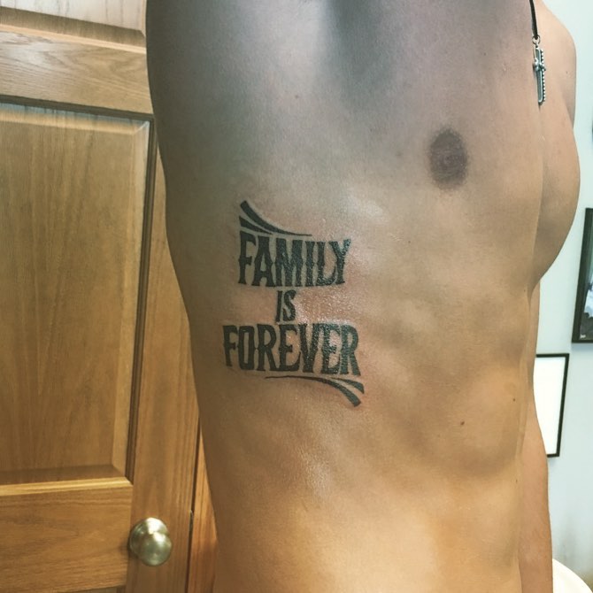 Tattoo on a person's side reads "FAMILY IS FOREVER," emphasizing the importance of family bonds.