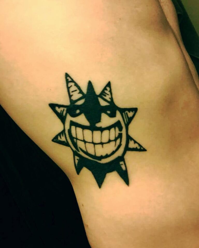 A black tattoo of a smiling sun with sharp spikes, located on the upper arm.