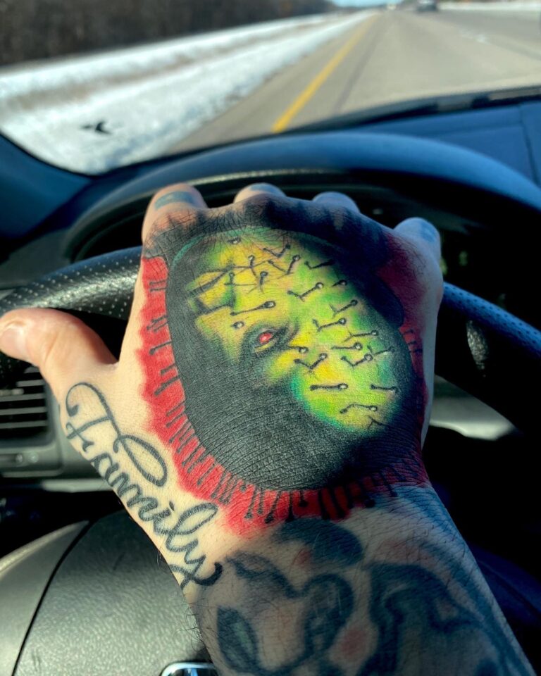 A colorful tattoo featuring a face with pins and the word "Family" on a hand gripping a steering wheel while driving.