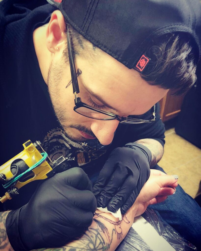 Tattoo artist focused on inking a design on a client's forearm in a studio setting.