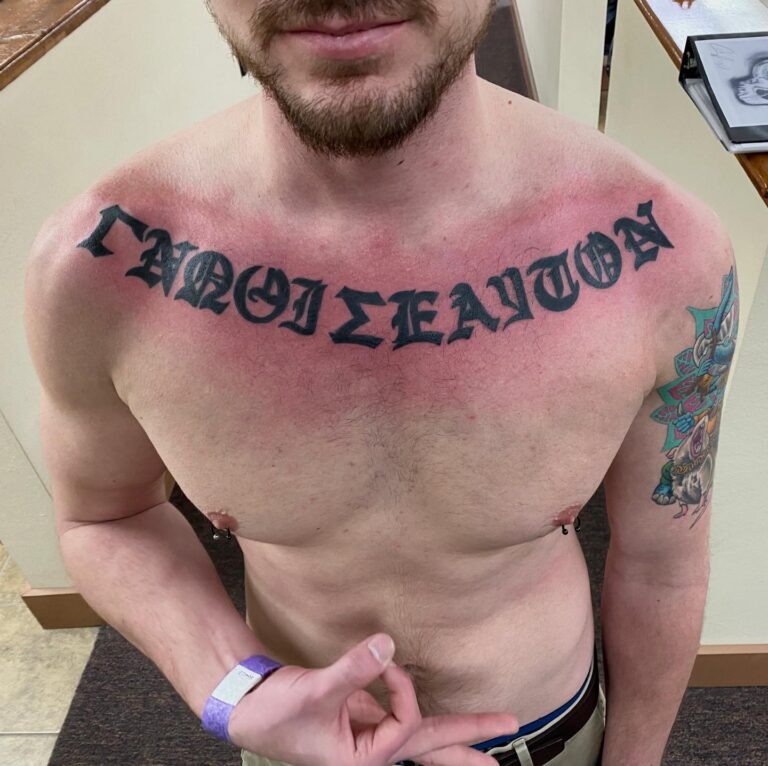 A man shows off a large black tattoo on his chest, with red skin indicating recent ink application.