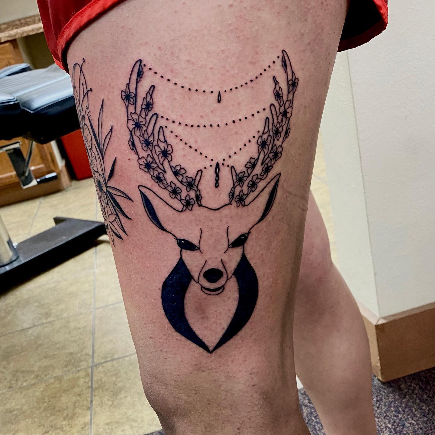 A detailed tattoo of a deer with floral antlers and geometric elements on a thigh.