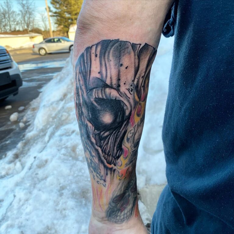 A detailed tattoo of a skull with vibrant colors on a person's forearm, set against a snowy background.