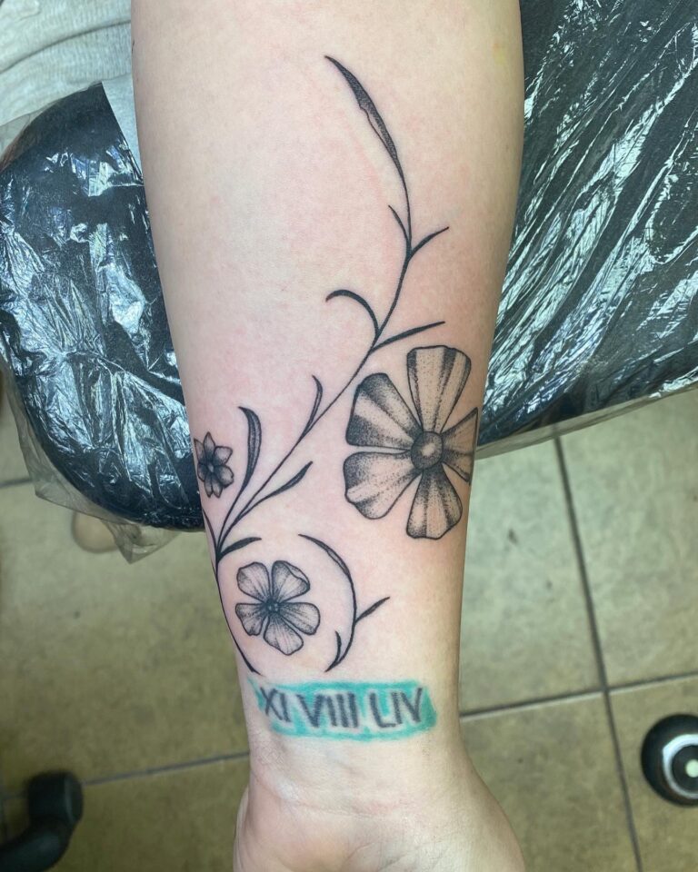 A tattoo featuring floral designs and Roman numerals on a person's forearm.