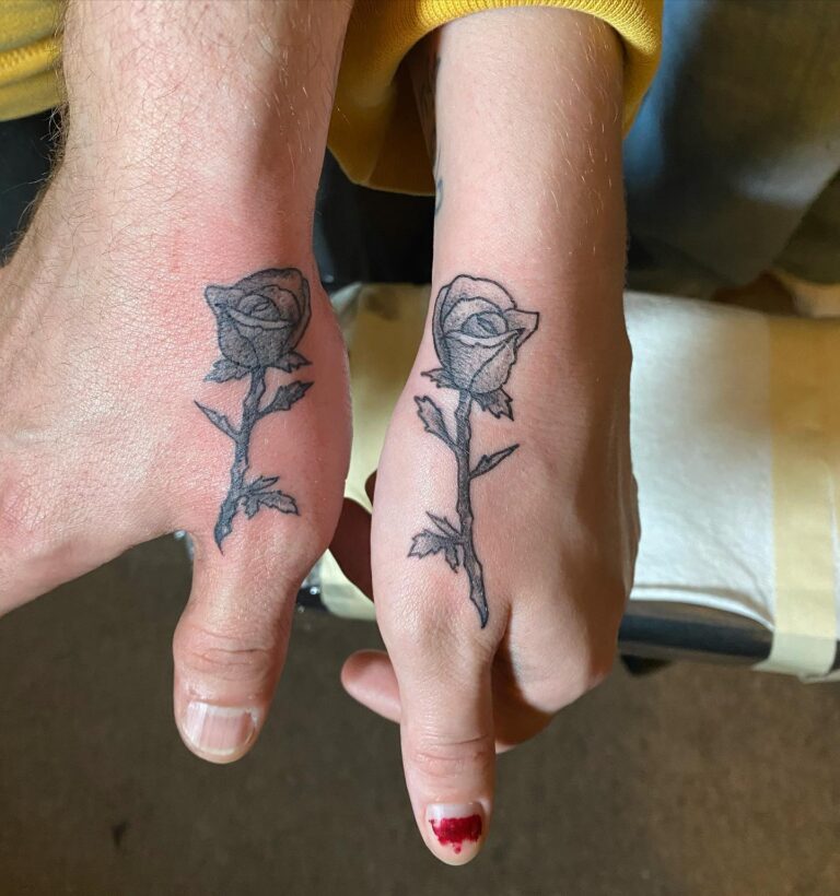 Two hands with matching black rose tattoos on the outer wrists, symbolizing connection and shared experience.