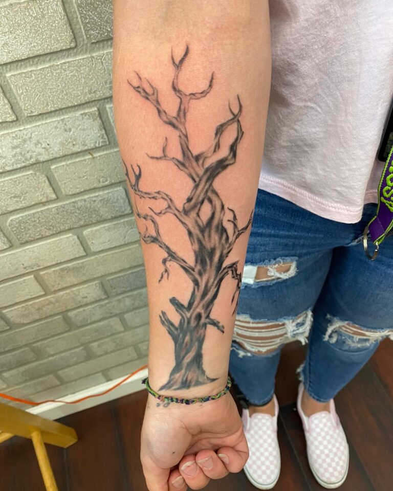 A detailed black and gray tattoo of a tree on a person's forearm, showcasing intricate branches and textures.
