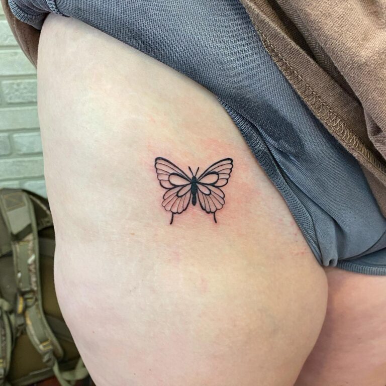 A delicate butterfly tattoo in black outline with soft pink accents on a person's thigh.