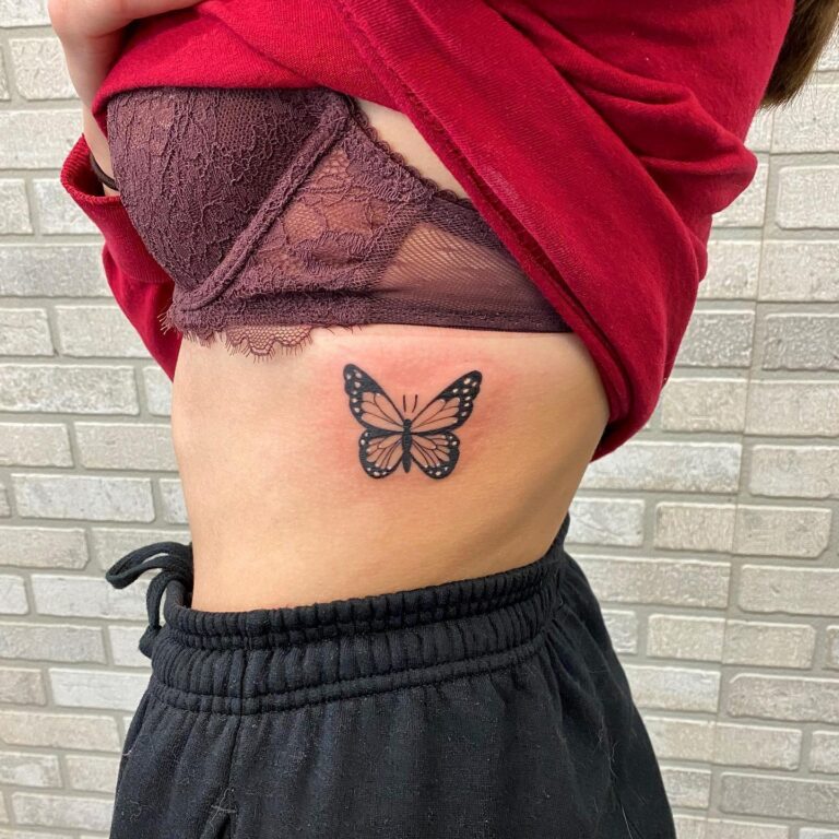 A butterfly tattoo is visible on the side of a person's torso, partially covered by a red shirt and black pants.