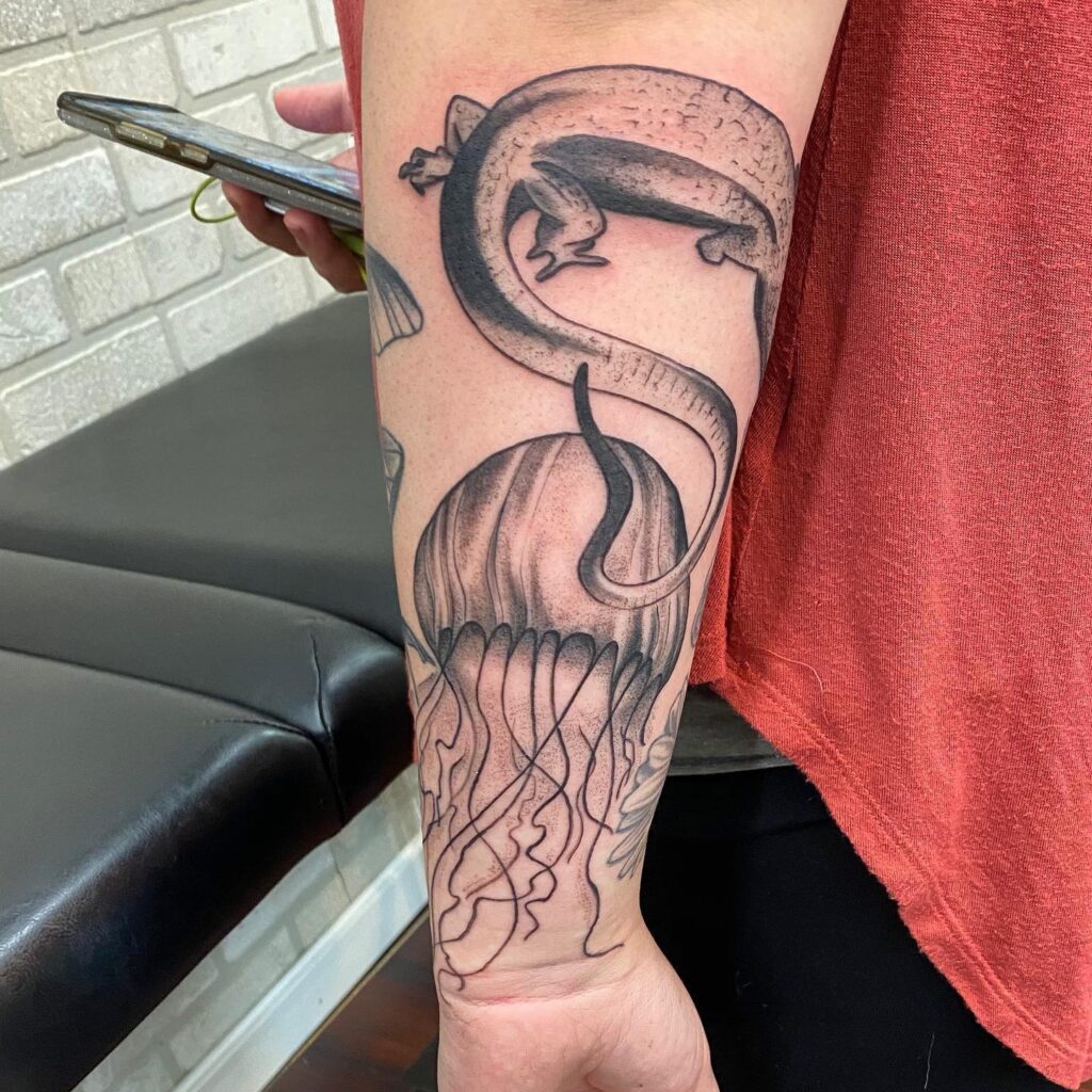 A detailed tattoo featuring a lizard entwined around a jellyfish on a person's forearm.