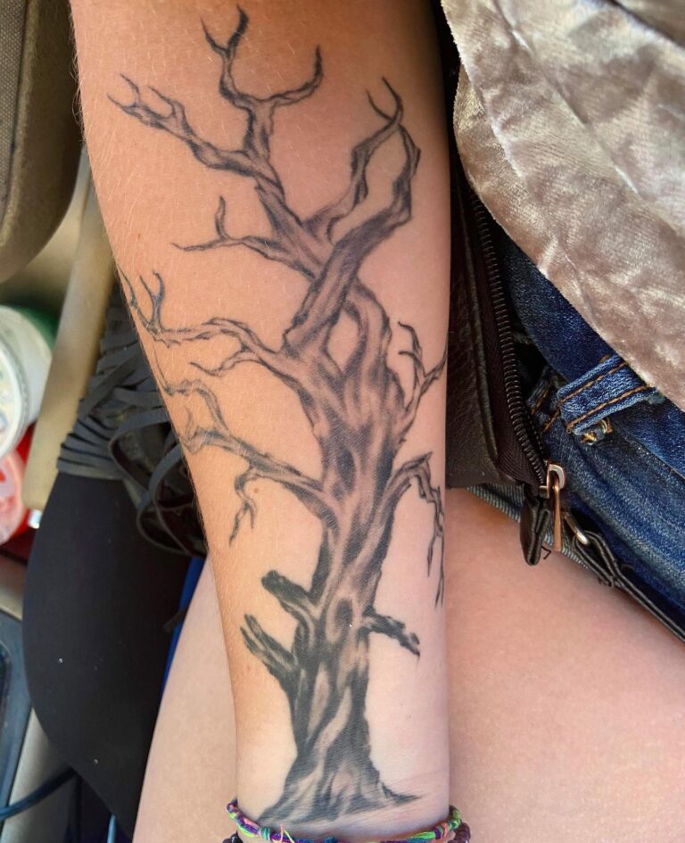 A detailed black and gray tattoo of a tree with intricate branches on a person's forearm.
