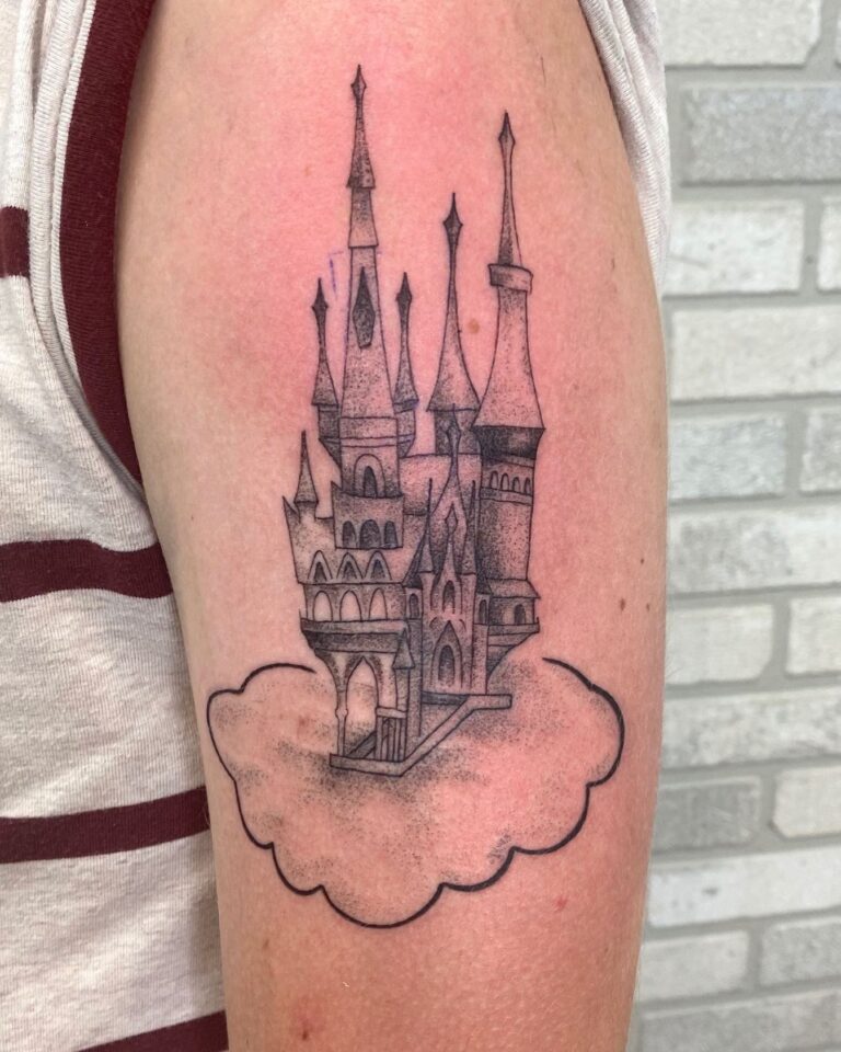 A detailed black and gray tattoo of a castle emerging from a cloud on a person's arm.