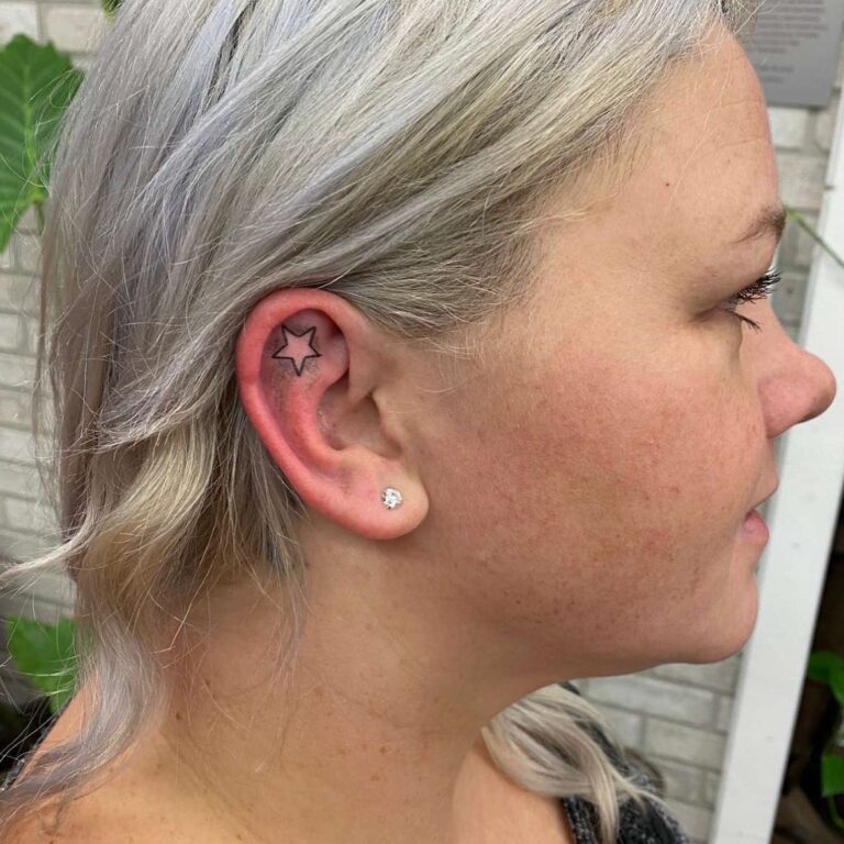 A woman with light blonde hair showcases a star tattoo behind her ear, accentuating her ear piercings.