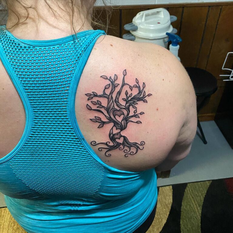 A detailed black ink tattoo of a tree with heart-shaped branches on the upper back of a person wearing a blue tank top.