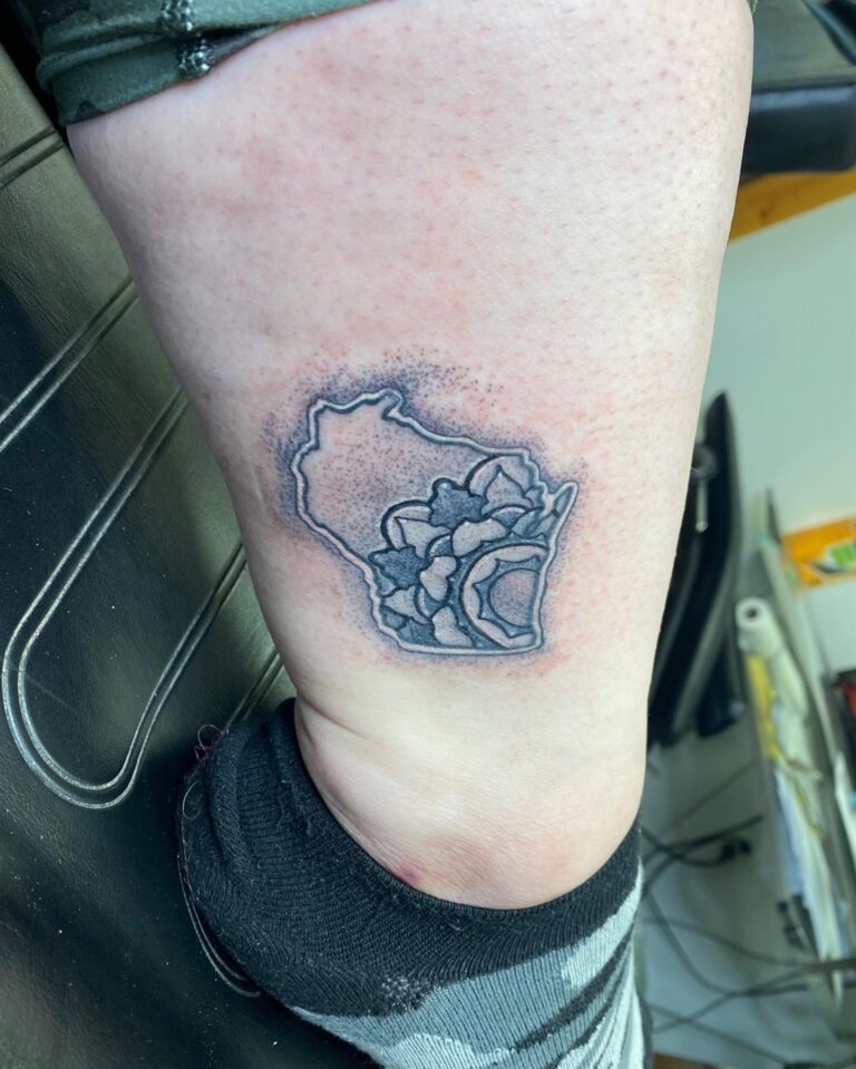 A tattoo featuring the outline of a state with a floral design, located on a person's ankle.