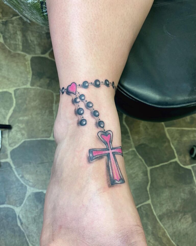 A tattoo of a black rosary with a pink heart and cross design on an ankle.