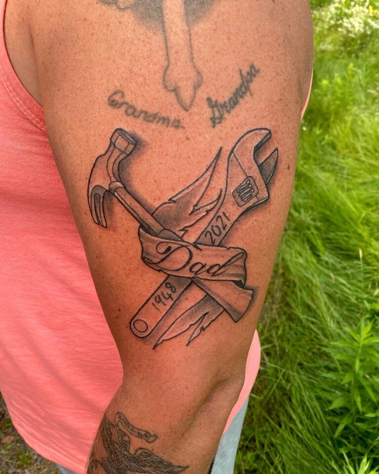 Tattoo featuring crossed tools and the word "Dad," with dates 1948 and 2021, symbolizing remembrance and tribute.