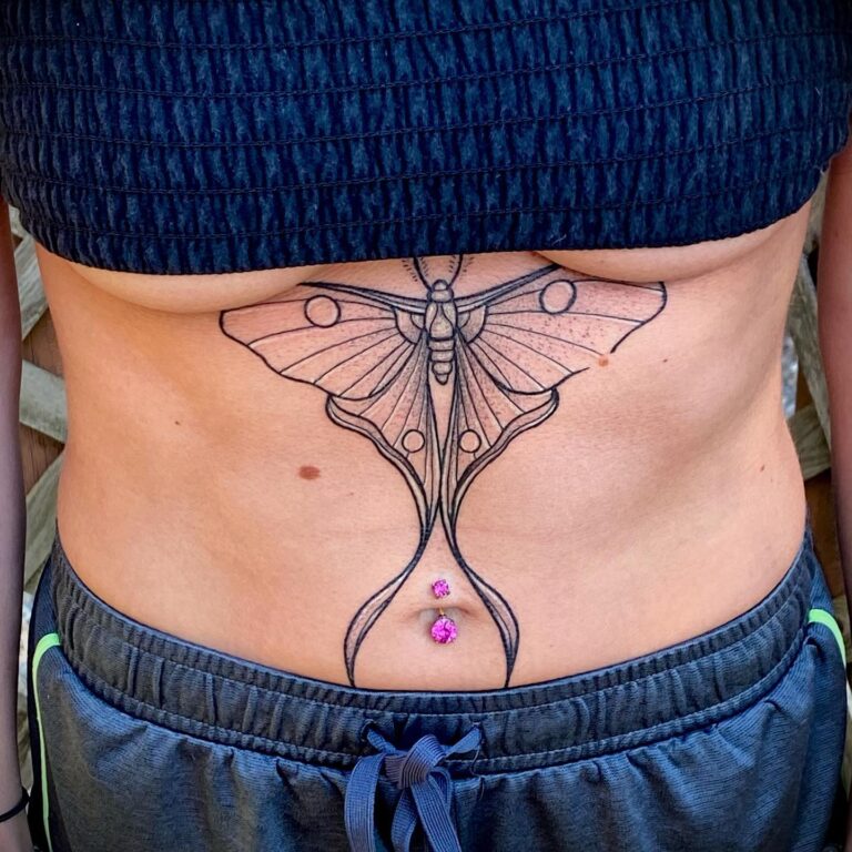 A detailed black moth tattoo adorns the abdomen, complemented by two pink gems near the navel.