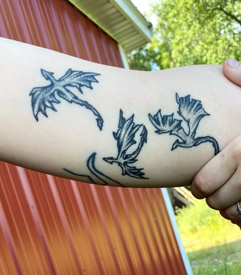 A close-up of a forearm tattoo featuring stylized dragons and leaves against a rustic red background.