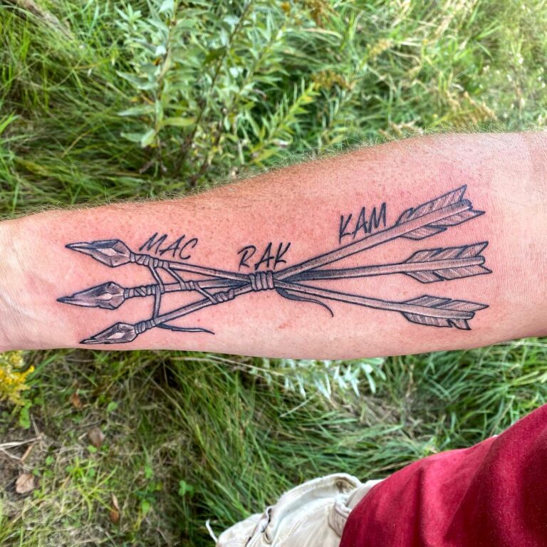 Tattoo on forearm featuring three arrows with the names MAC, RAK, and KAM inscribed alongside them.