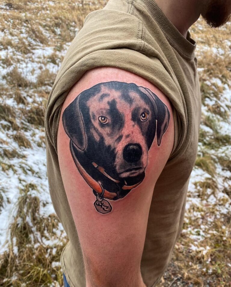 A detailed tattoo of a dog's face on a man's upper arm, showcasing realistic features and a collar.