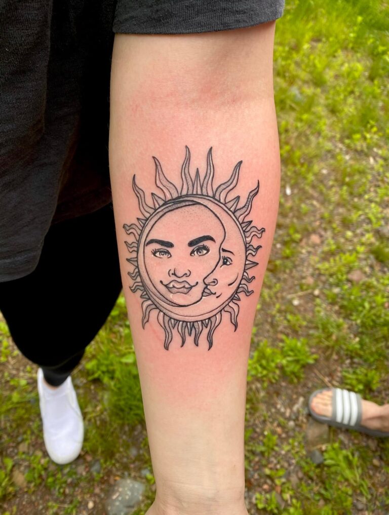 Tattoo featuring a sun and moon design with facial features, inked on a person's forearm against a grassy background.