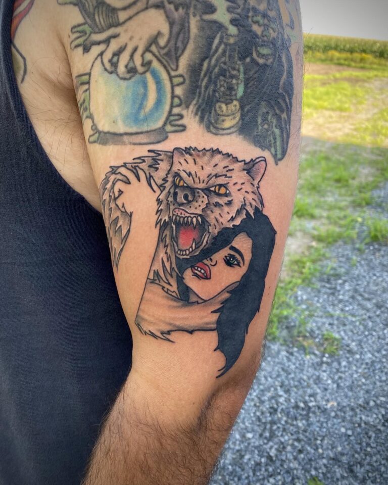 A detailed tattoo on an arm featuring a fierce wolf and a woman with dark hair, conveying a sense of intensity and emotion.