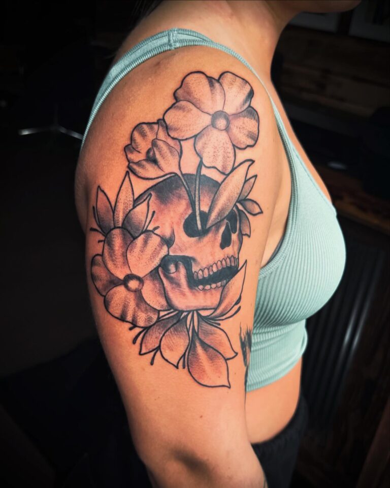 A detailed tattoo featuring a skull surrounded by flowers on a person's upper arm.
