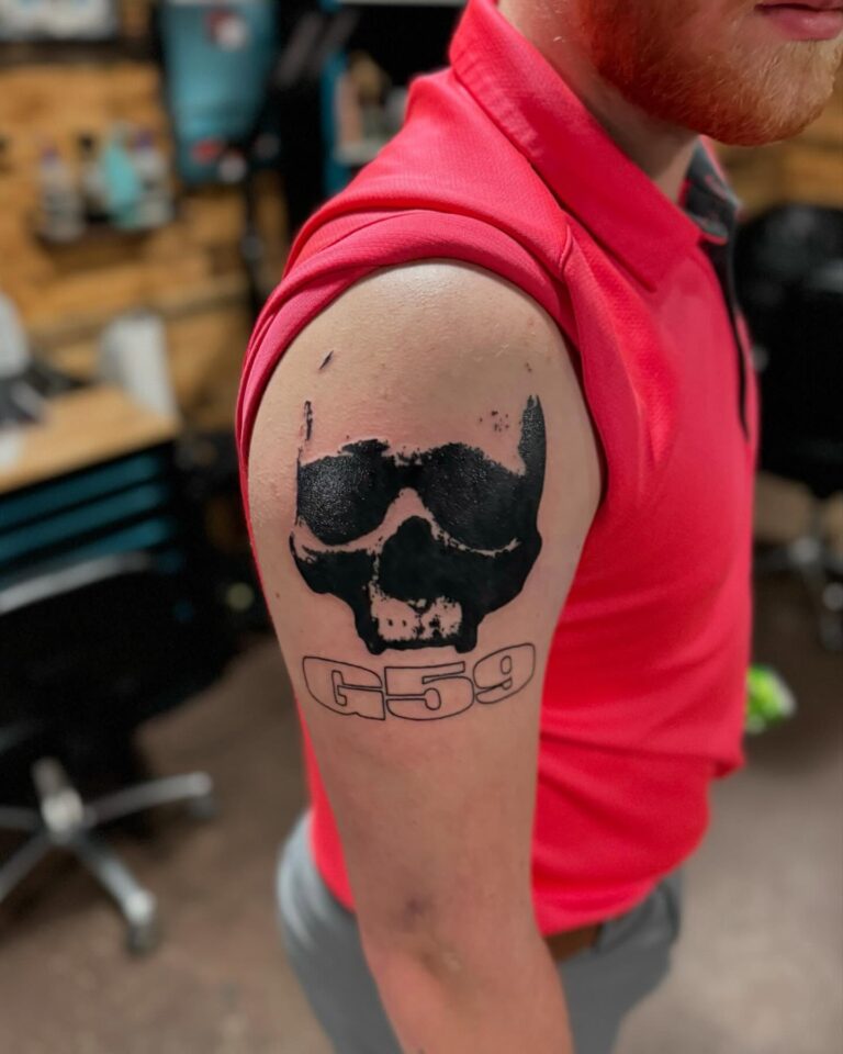 A person in a red shirt displays a tattoo of a skull with the text "G59" on their upper arm.
