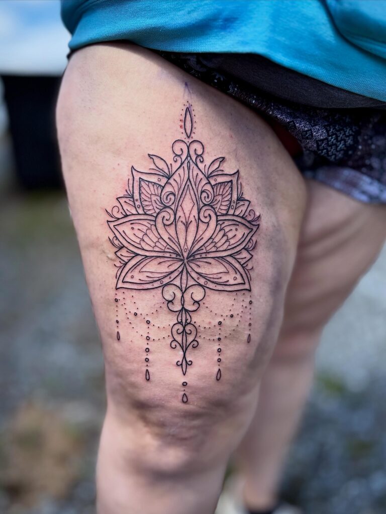 Intricate black line tattoo of a lotus flower with decorative elements on a thigh.